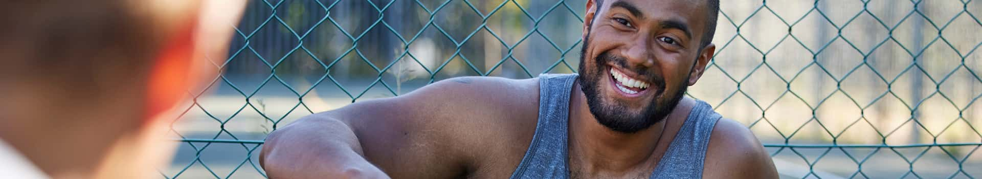 Person leaning against wire fence smiling.