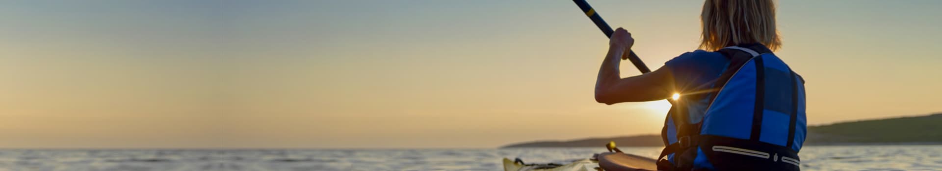 Person rowing in Kayak with backpack and sun in the background