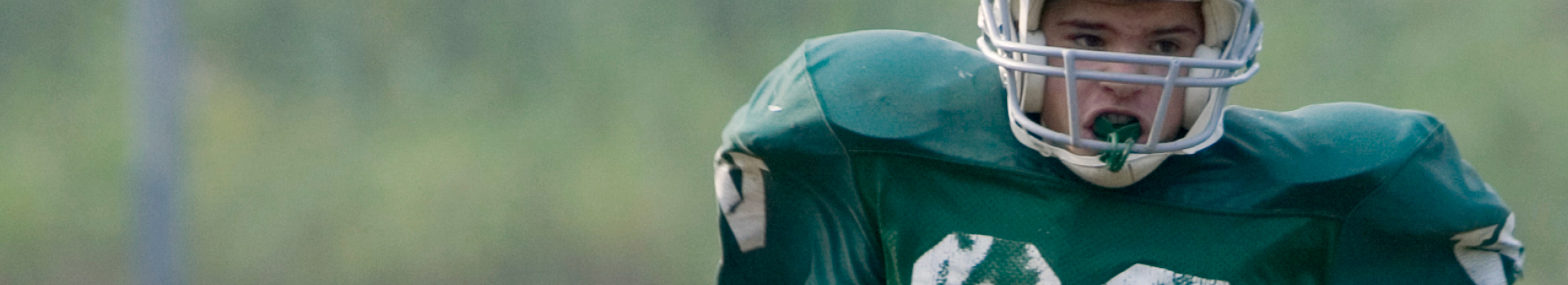 Youth football player in green uniform with helmet on.