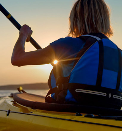 Person rowing in Kayak with backpack and sun in the background