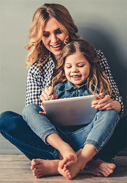 Woman with little girl on her lap looking at an Ipad or computer screen