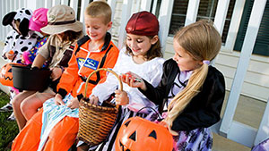 a-group-of-children-in-Halloween-costumes-sitting-on-a-bench-looking-at-their-candy-and-treats