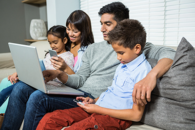 Family looking at electronic devices while sitting on couch
