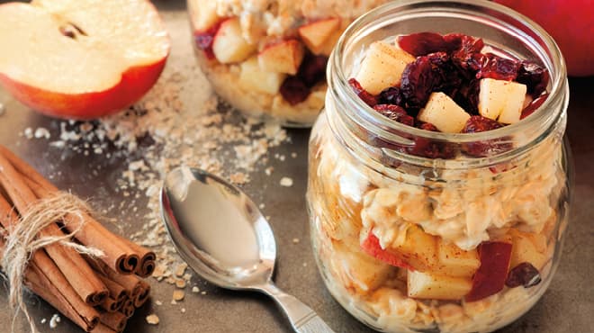 Overnight oats in a jar with a spoon, cinnamon sticks and cut apple