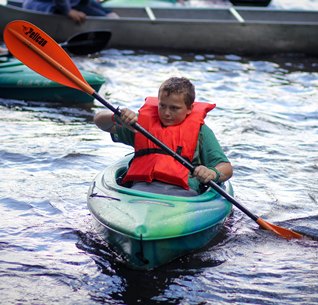 young boy paddling in kayak with life jacket