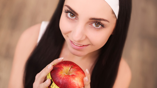 Young woman holding an apple with measuring tape