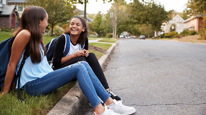 Teen girls sitting on curb smiling