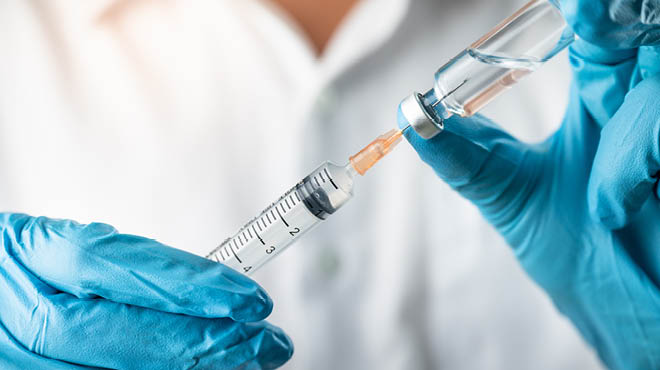 gloved hands filling vaccine syringe