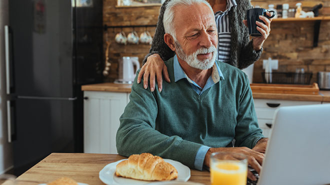 Grey haired man on laptop having breakfast