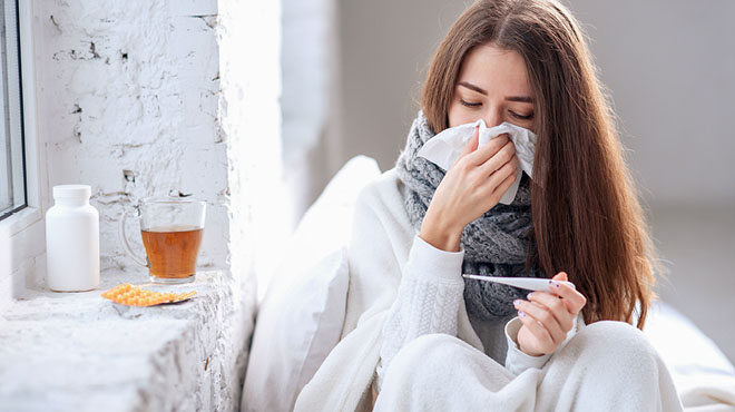 Young woman taking her temperature and blowing her nose