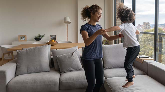 child jumping on sofa holding moms hands