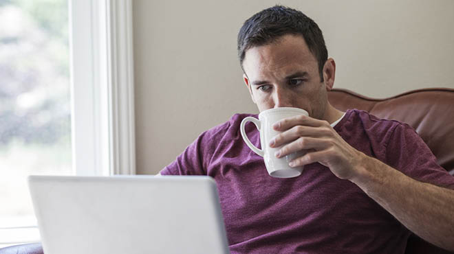 Person drinking from mug while sitting and looking at laptop
