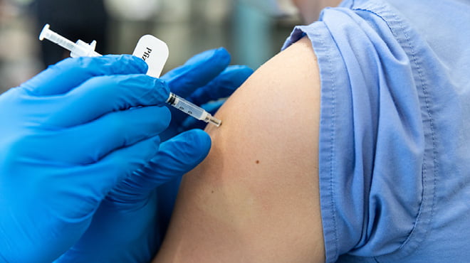 Gloved hands giving vaccination in upper arm