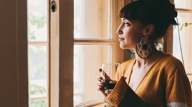 Person holding wine glass, looking out window, large earrings, hair up
