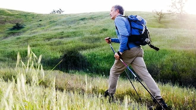 Open trail hiking using walking poles and wearing backpack