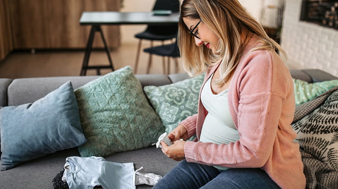 Pregnant woman folding baby clothes on sofa