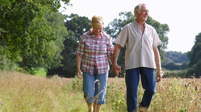 Senior couple walking in field while holding hands