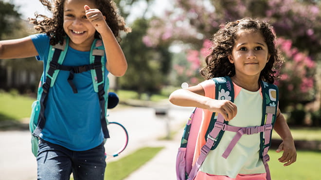 Two kids with backpacks running to school