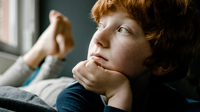 Red-headed child lying on bed resting head on hand