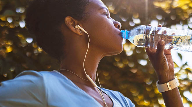 Drinking bottled water, wearing earbuds