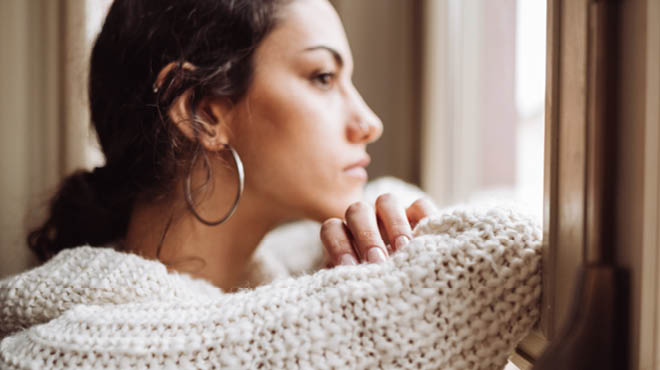 Wearing ivory knit sweater and hoop earrings, looking out window