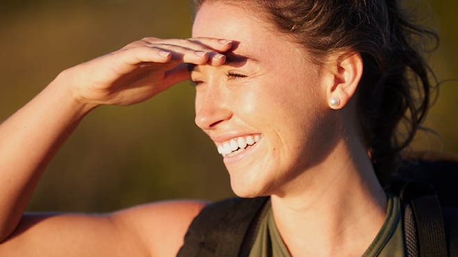 Smiling person shielding sun from eyes with hand