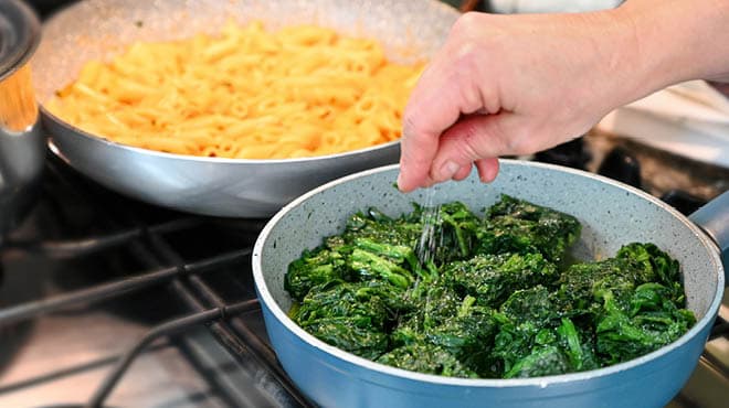Sprinkling salt on broccoli next to pan of mac and cheese
