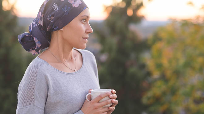 Person wearing head scarf, holding coffee cup while outdoors