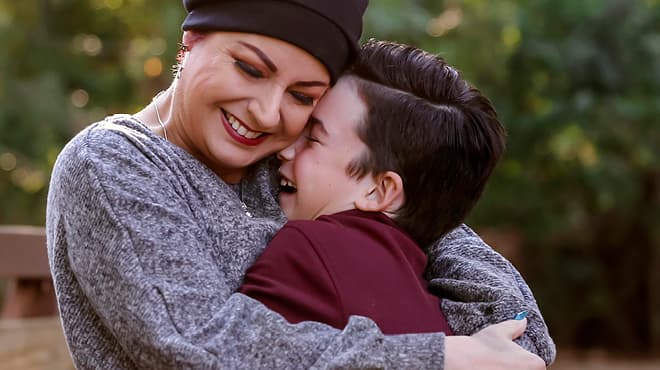 Adult wearing chemo cap hugging child