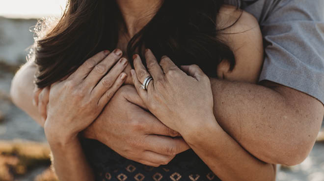 Couple with arms clasped around person in front