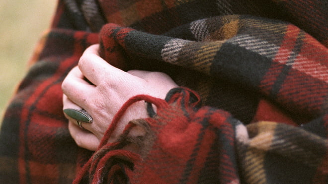 Person's hand holding plaid blanket close to their body