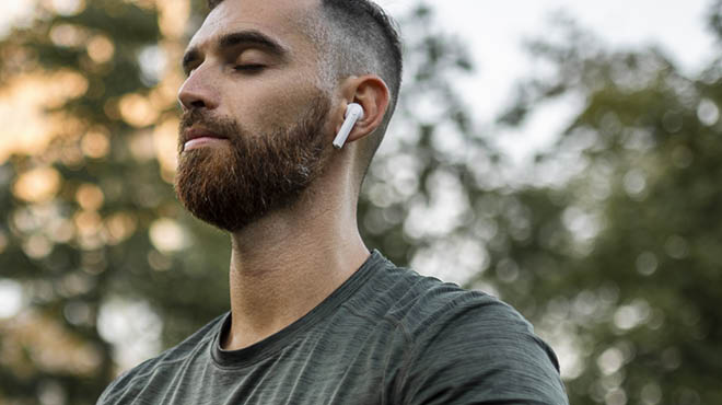 Person outdoors with eyes closed, using earbud