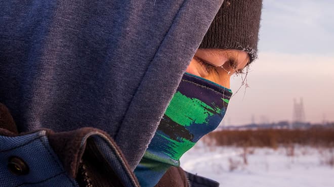 Person outdoors in the cold wearing hat, hoodie and facemask