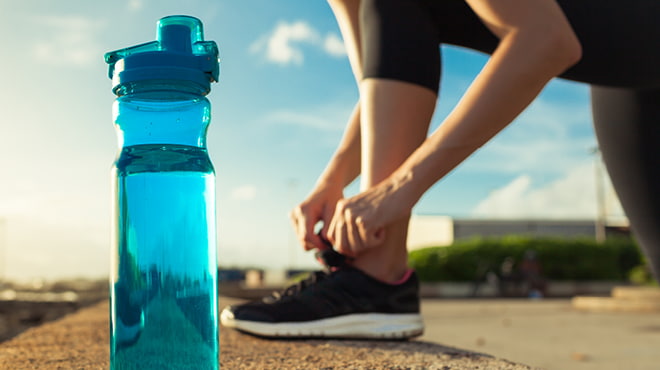 Close-up of water bottle and person tying athletic shoe