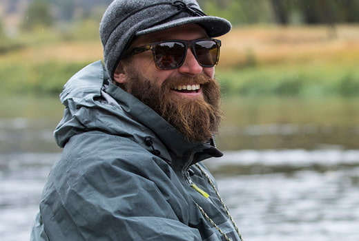 Person wearing waterproof gear, hat and sunglasses near a lake
