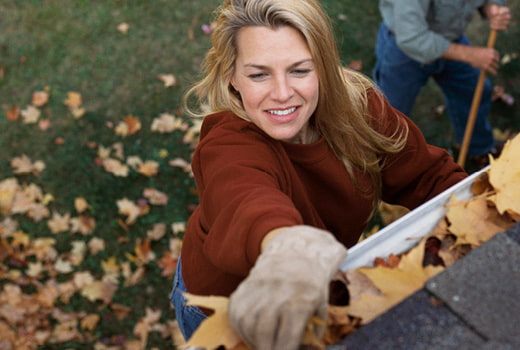 Person on ladder cleaning leaves from rain gutter