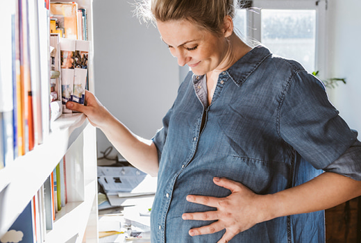 Pregnant lady with hand on stomach pulling files from a shelf