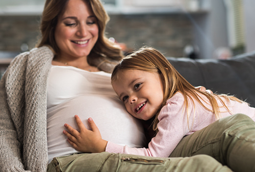 Pregnant woman with young girl hugging her stomach