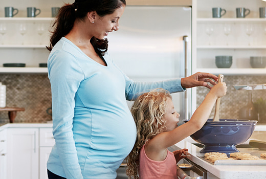 Pregnant woman with young girl mixing something in bowl
